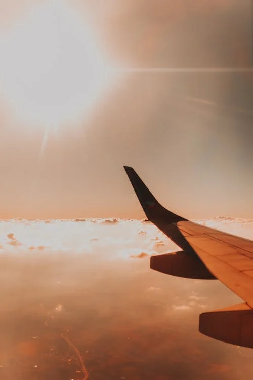 Airplane wing above clouds against bright sun