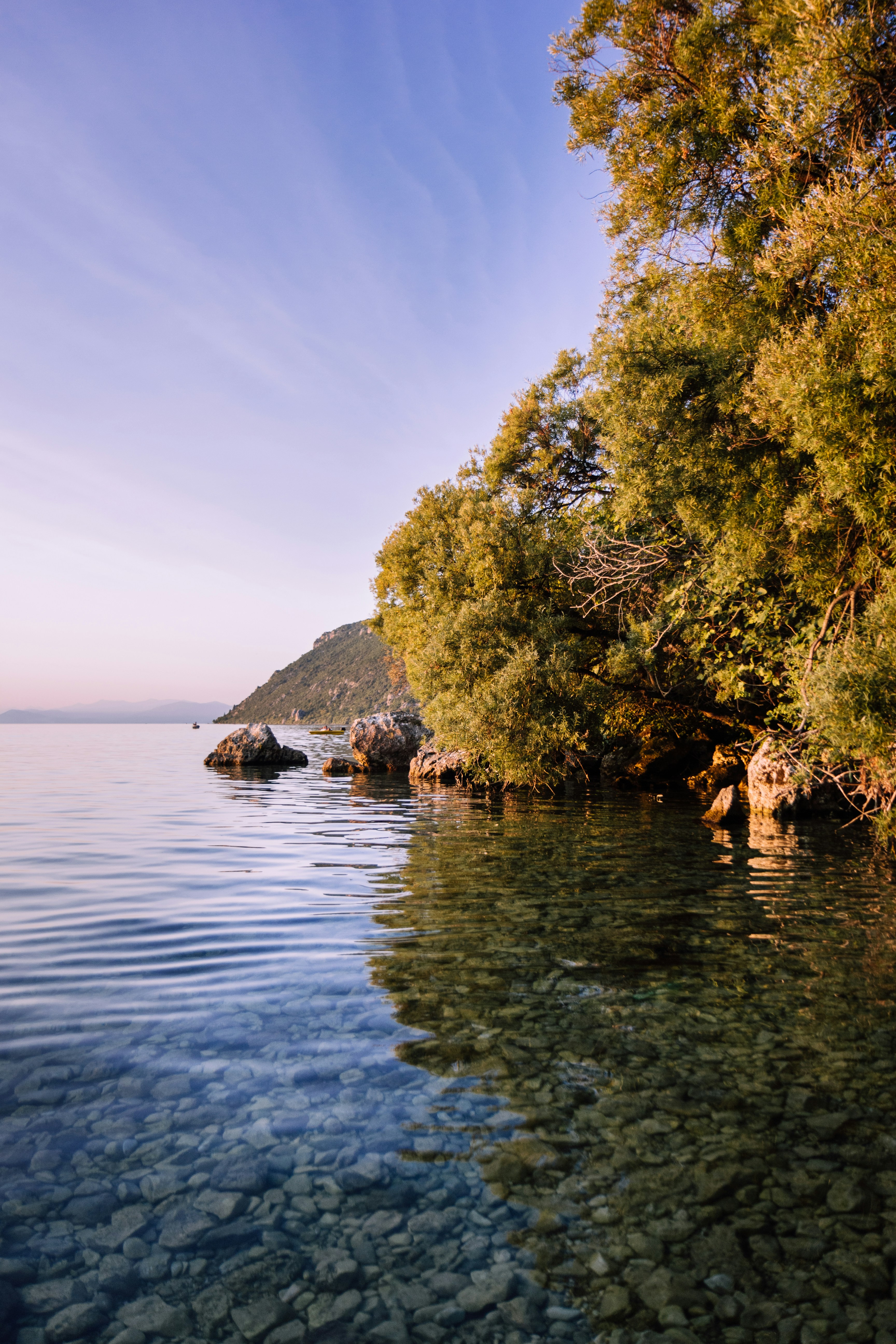 Purple hour shot of Ohrid Lake's still water on a rocky beach.